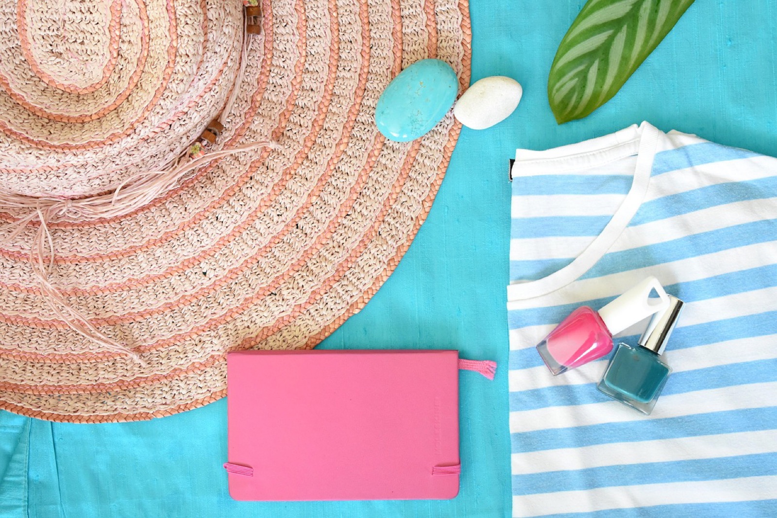 Pink and teal nail polish on a summer beach towel beside a straw hat