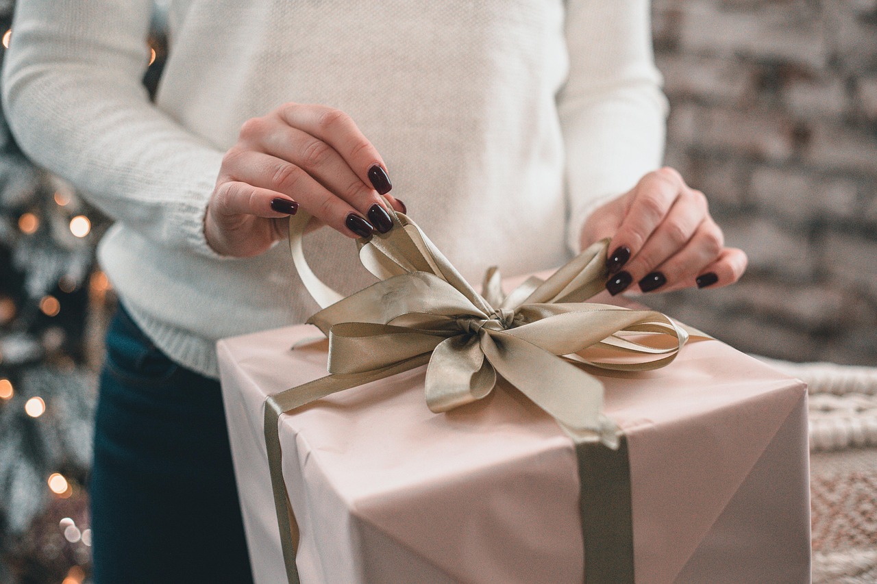 Hands with dark painted nails tying the ribbon on a gift